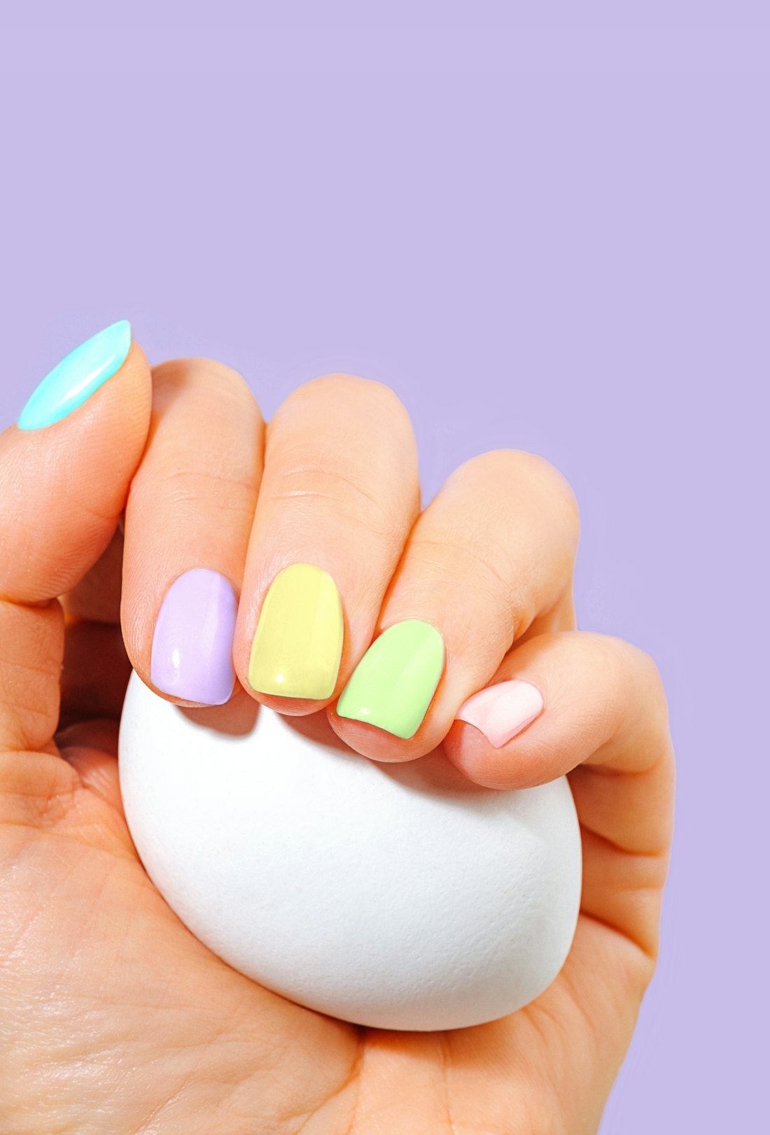 Elegant woman's hand with pastel color manicure holding a white egg. Easter Holiday composition. Sty...
