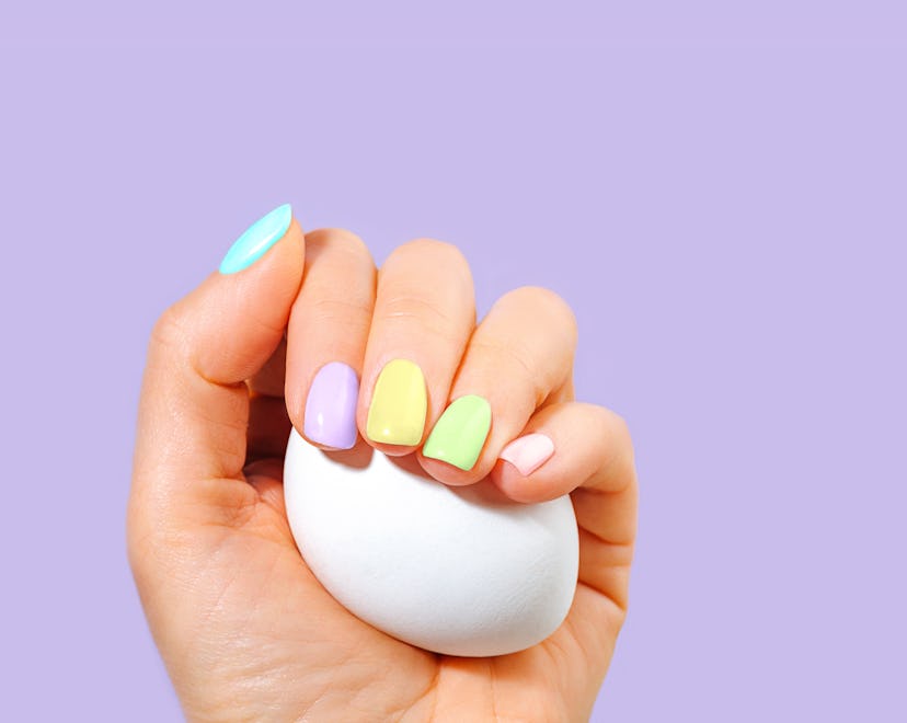 Elegant woman's hand with pastel color manicure holding a white egg. Easter Holiday composition. Sty...