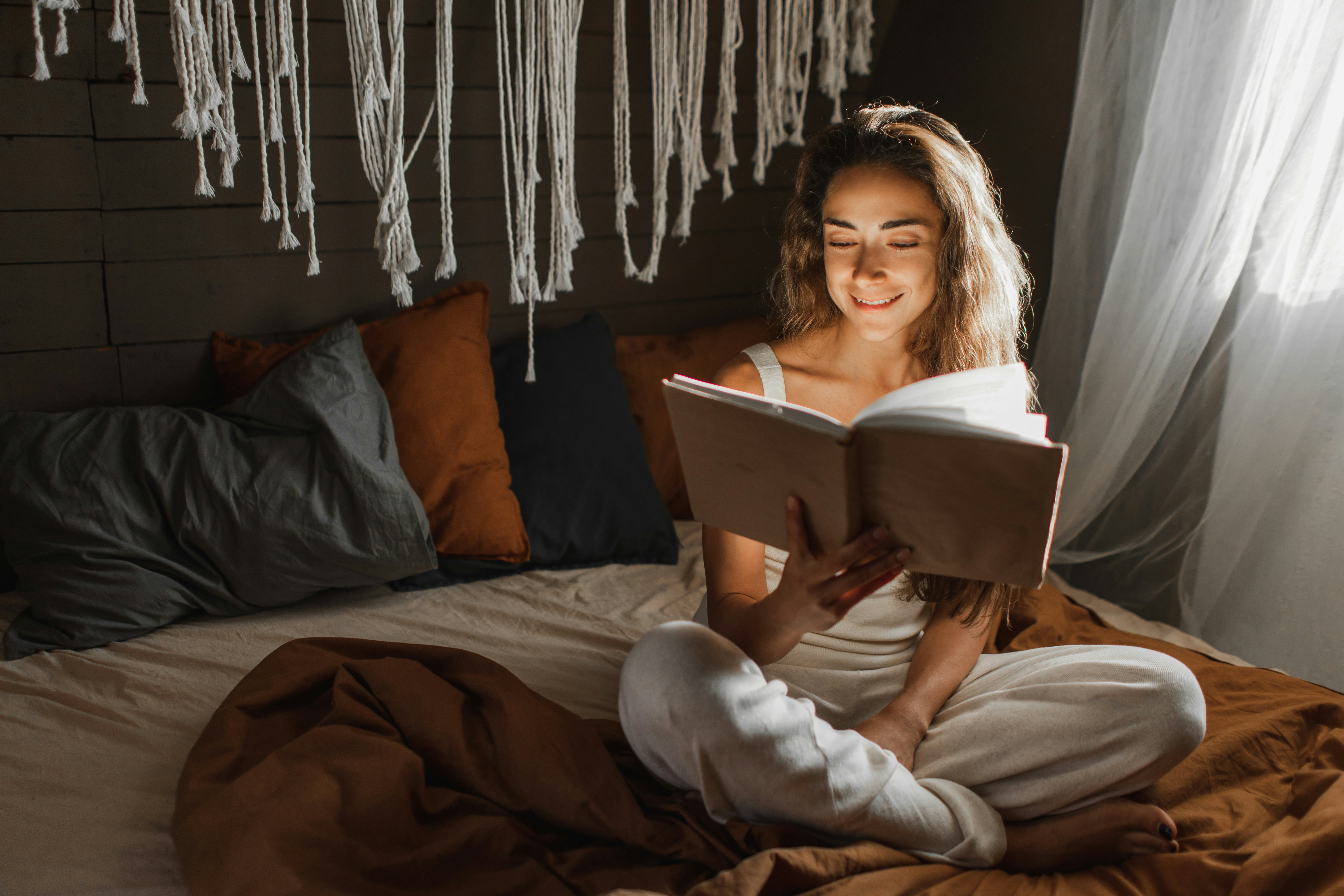 Woman relaxing and reading book on cozy bed in cozy loft. Reading and learning for adult beautiful f...