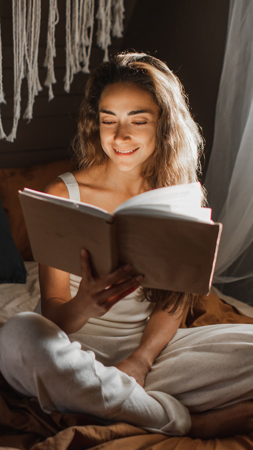 Woman relaxing and reading book on cozy bed in cozy loft. Reading and learning for adult beautiful f...