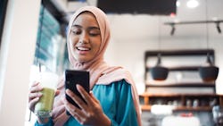 A woman wearing a pink hijab and drinking a green smoothie reads Twitter. Does twitter have an edit ...