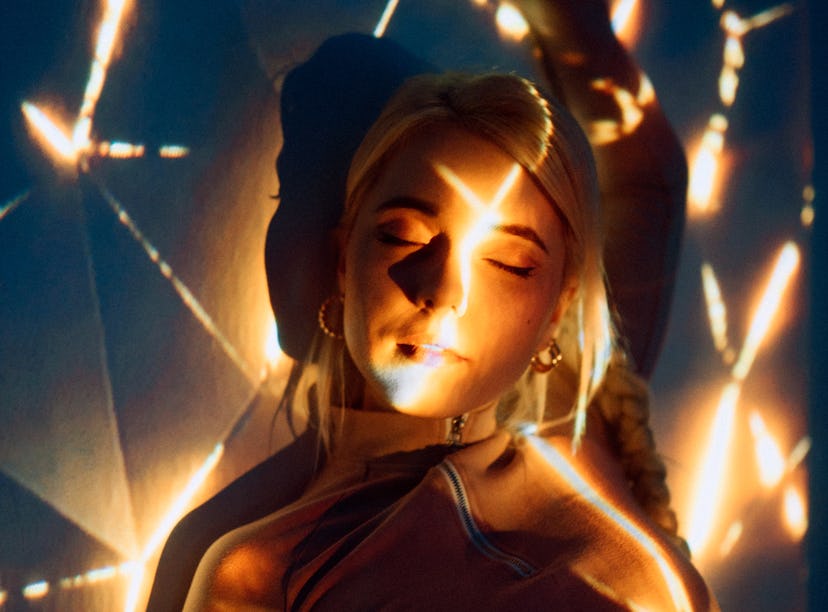 Young woman basking in bright lights, embracing the April 18, 2022 weekly horoscope for her zodiac s...