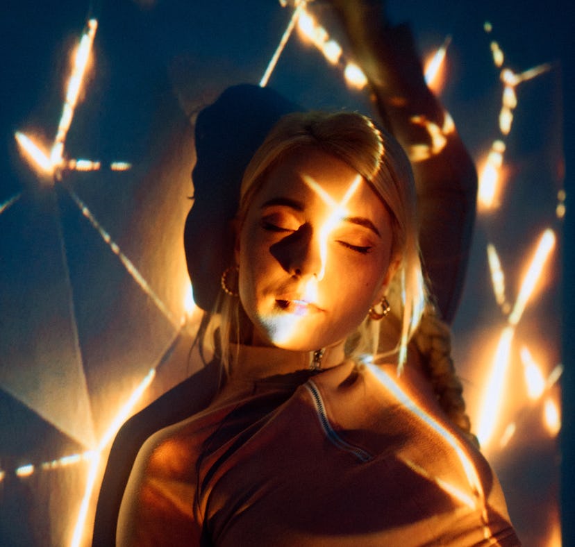 Young woman basking in bright lights, embracing the April 18, 2022 weekly horoscope for her zodiac s...
