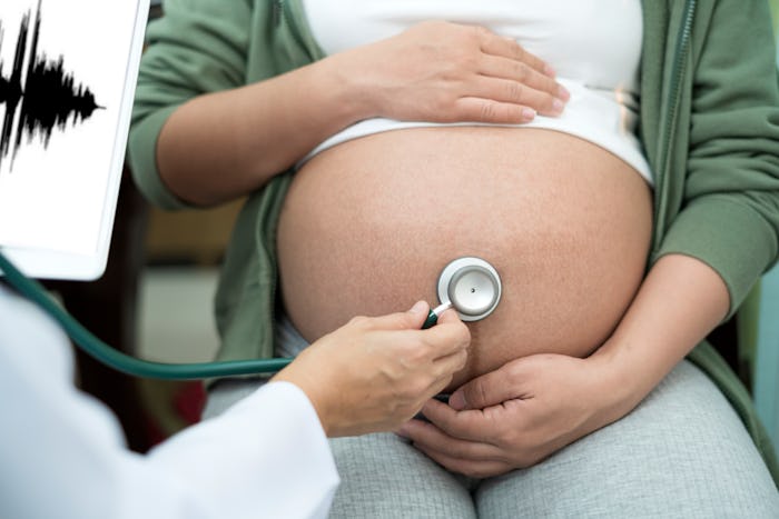 Shot of Doctor listening breath of baby in pregnant woman abdomen.