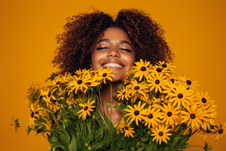 Young woman smiling over a bouquet of daisies, relishing the April 25, 2022 weekly horoscope for her...