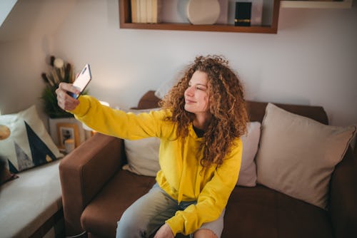 A woman with curly hair sits on a sofa and uses a cell phone for a video call. Here's how to see you...