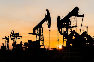 The silhouette of several oil pumps on a beautiful sunset sky with sun setting in between them.Siber...