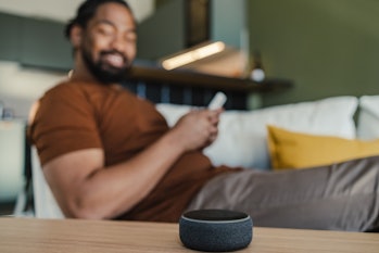 man sitting on the couch and using his smart speaker and mobile phone