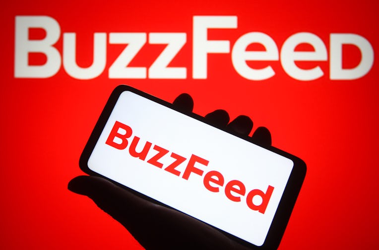 UKRAINE - 2021/12/18: In this photo illustration, BuzzFeed Inc. logo is seen on a smartphone and a c...