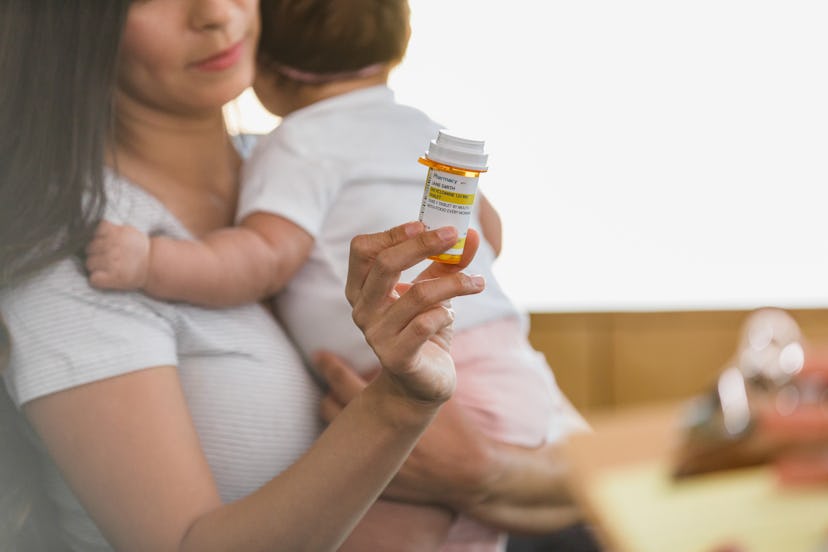 a postpartum mom with a new baby holds a bottle of medication for her postpartum infection