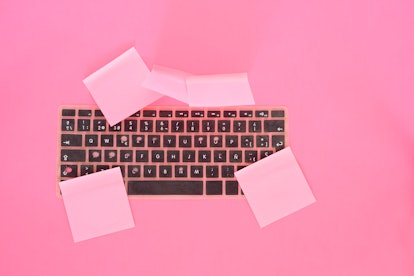 A plastic keyboard with pink adhesives notes in a pink color background.