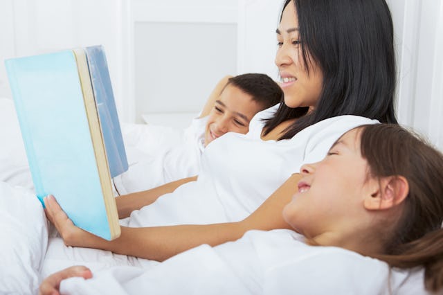 Smiling multiracial family reading story book laying in bed.
