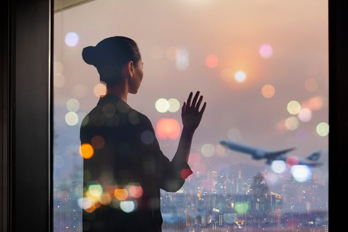 Young Chinese woman standing at airport terminal departure area window waving to airplane, China