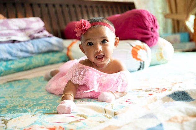 Infant girl relaxing on parents' bed while dressed in pink fancy clothes, baby girl names that start...
