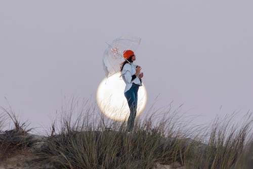A woman stands with a clear umbrella in front of the full moon. These may 2022 full flower moon  rit...