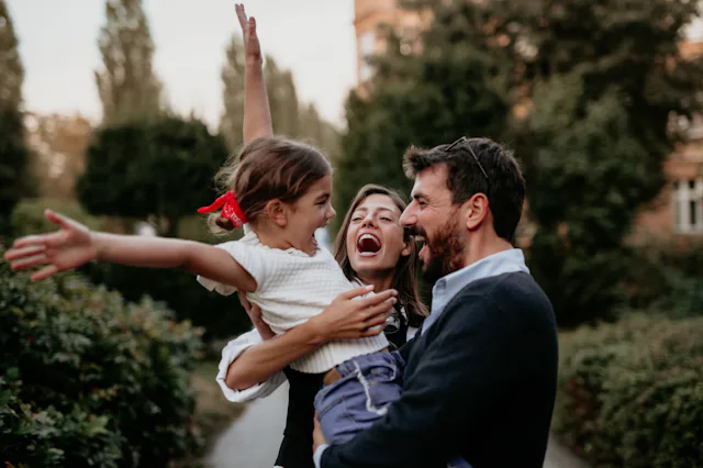 Happy dad and mom with their cute daughter hug and have fun walking outdoors after their work.