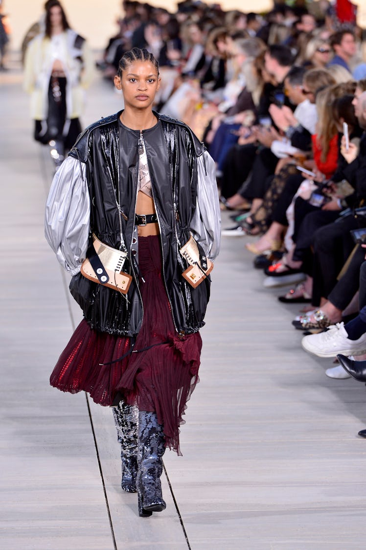 A model walking the runway for the Louis Vuitton's 2023 Cruise Show in a black and silver jacket and...