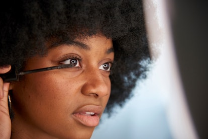 Close-up view of an Afro woman applying mascara on her eyelashes while doing her makeup. Concept of ...