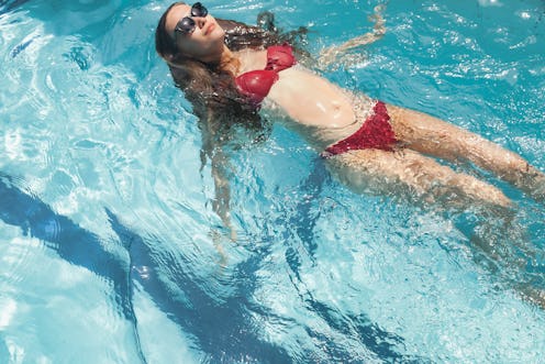 Young slim woman in swimsuit swims in swimming pool. Cute female relaxing and resting in swimming po...