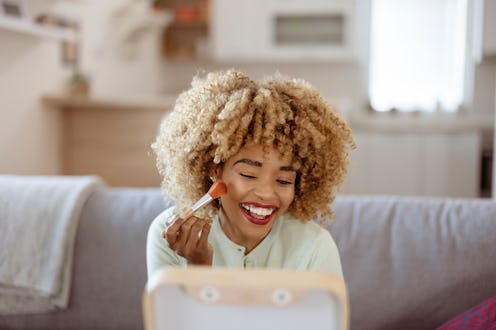 Beautiful African American woman with mirror applying makeup at home