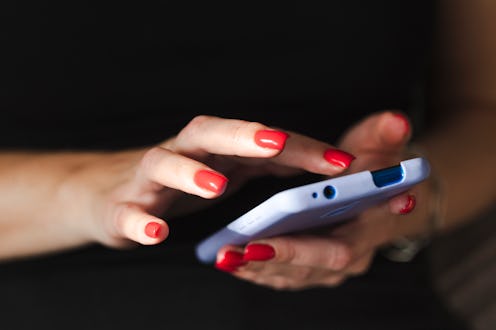 Young millennial woman texting on mobile device. Hands of a woman wearing bright red nail polish in ...