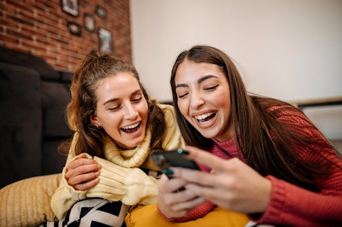 Best friends lie on the floor in the living room and use a mobile phone