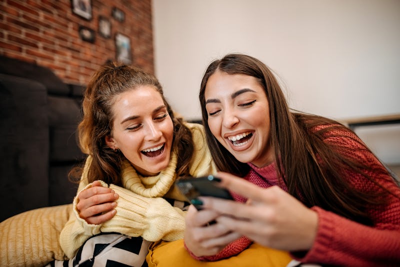 Best friends lie on the floor in the living room and use a mobile phone