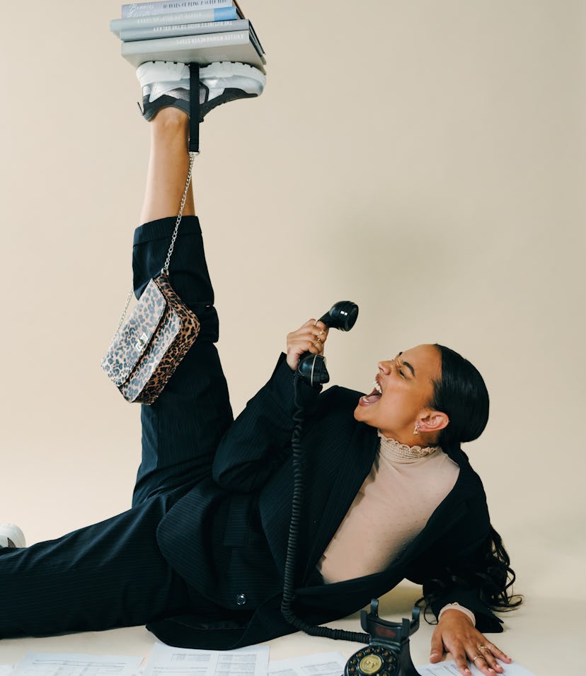 young woman yells into phone as she balances books on her foot and poses for a 2022 new moon in gemi...