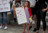 A girl in Wilkes-Barre, PA eats potato chips while holding a sign at an abortion rights rally readin...