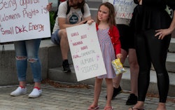 A girl in Wilkes-Barre, PA eats potato chips while holding a sign at an abortion rights rally readin...