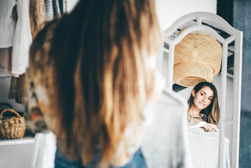 A woman looks at clothes in a mirror. Here's your daily horoscope for May 19 2022.