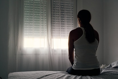 A woman sitting on her back and looking through a window who has a healthy relationship with her pas...