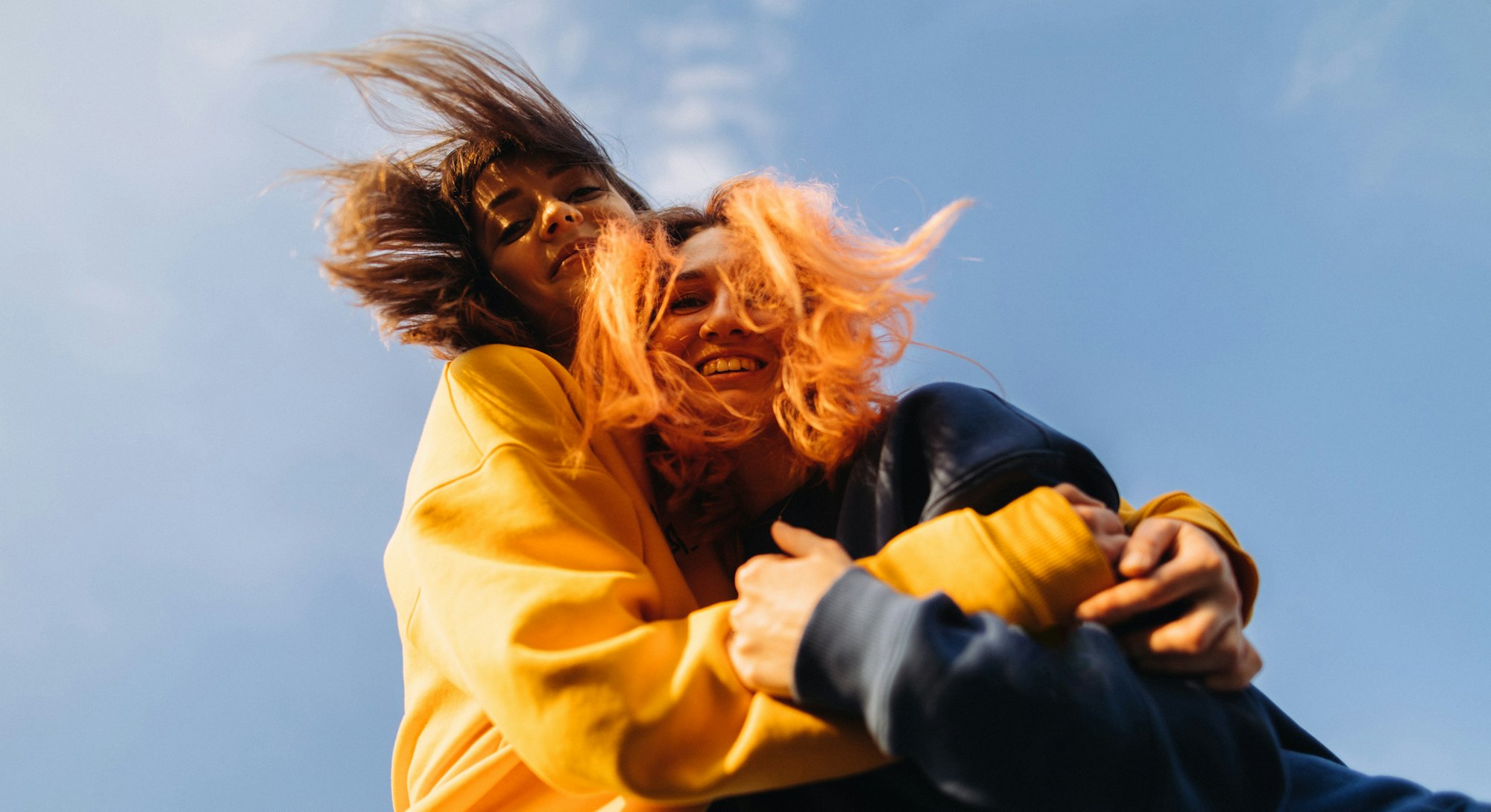 Two women hugging at the blue sky background at the sunset