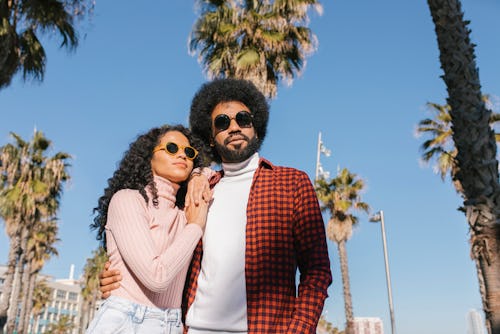 A couple in sunglasses against palm trees. here's your daily zodiac sign for may 20.