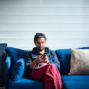 A man on a blue sofa uses smartphone.