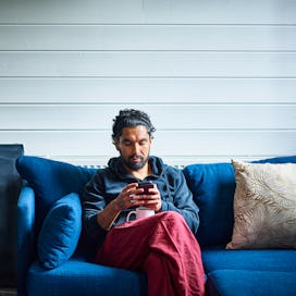 A man on a blue sofa uses smartphone.