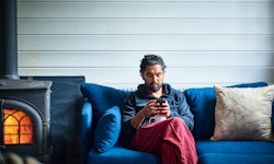 A man on a blue sofa uses smartphone.