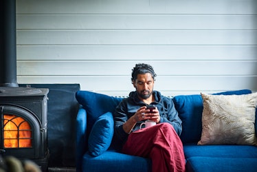 一个坐在蓝色沙发上的男人在用智能手机。