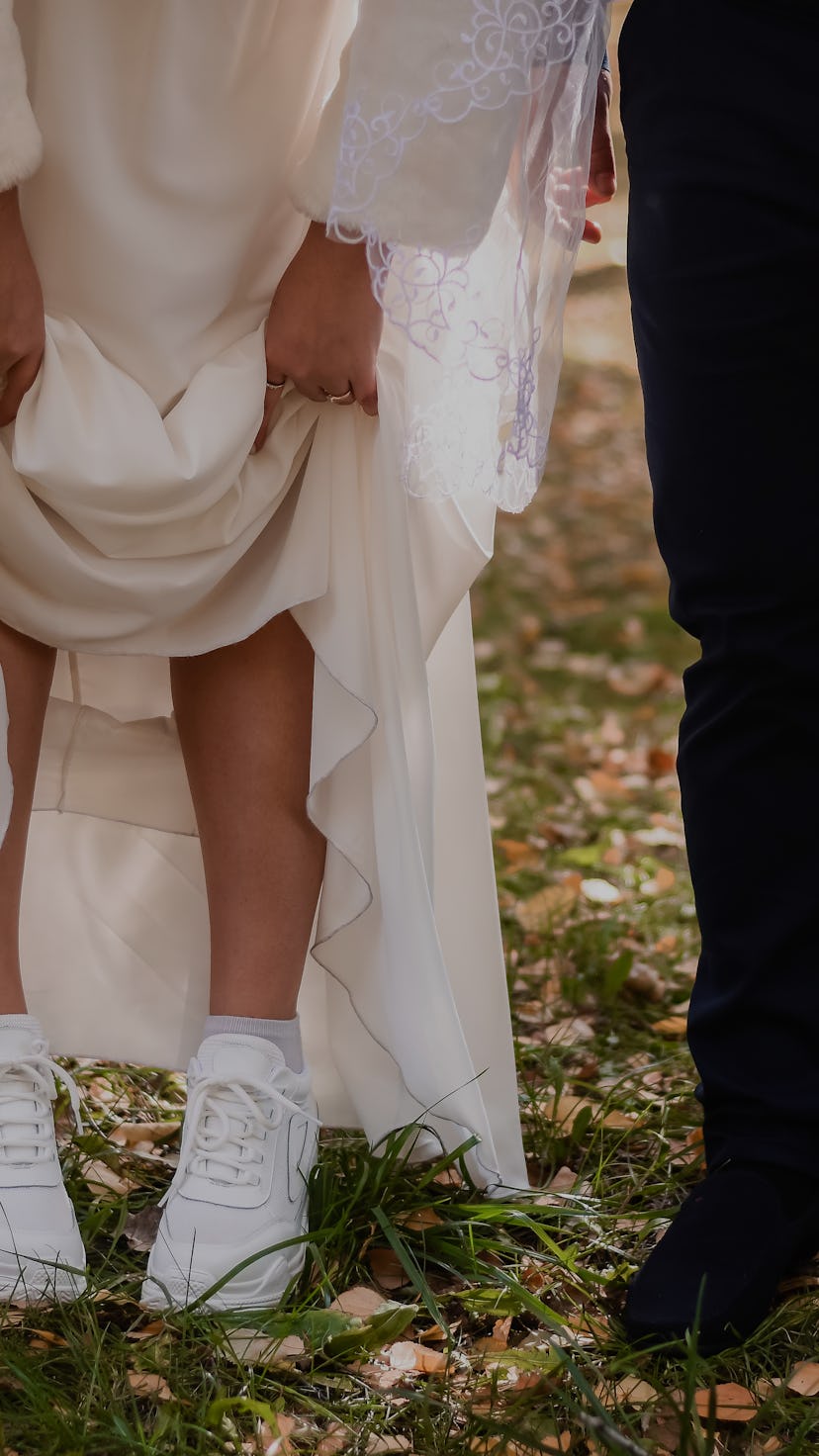 the bride and groom with a bouquet of flowers in fall in the park. the bride lifted her skirt, showi...