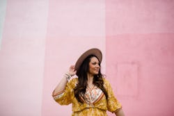 A woman smiles against a pink wall. Your may 3 zodiac sign daily horoscope for 2022.