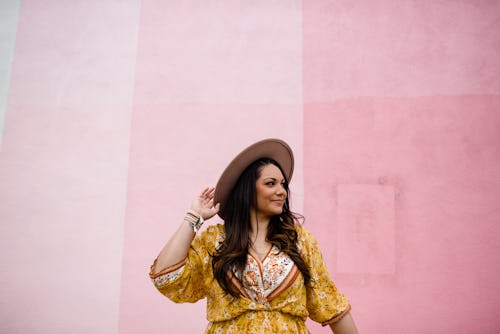 A woman smiles against a pink wall. Your may 3 zodiac sign daily horoscope for 2022.