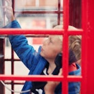 Two little boys trying to use a telephone in an old fashioned phone box