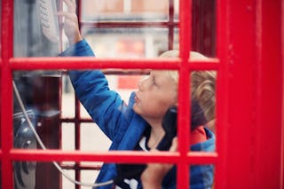 Two little boys trying to use a telephone in an old fashioned phone box