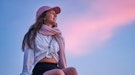 young woman wearing a pink hat gazes at the sunset as she thinks about the astrology of may 16, 2022