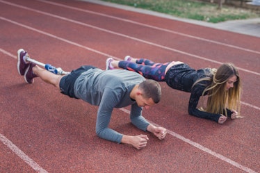 28 years old couple is training outdoors. They are doing plank exercise to build their core