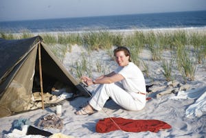 A woman sits in front of a small tent on the beach while camping on Fire Island, New York, 1955. (Ph...