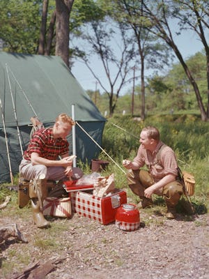 A father and son help themselves to sandwiches from their Kiltie coolbox during a camping trip, 1956...