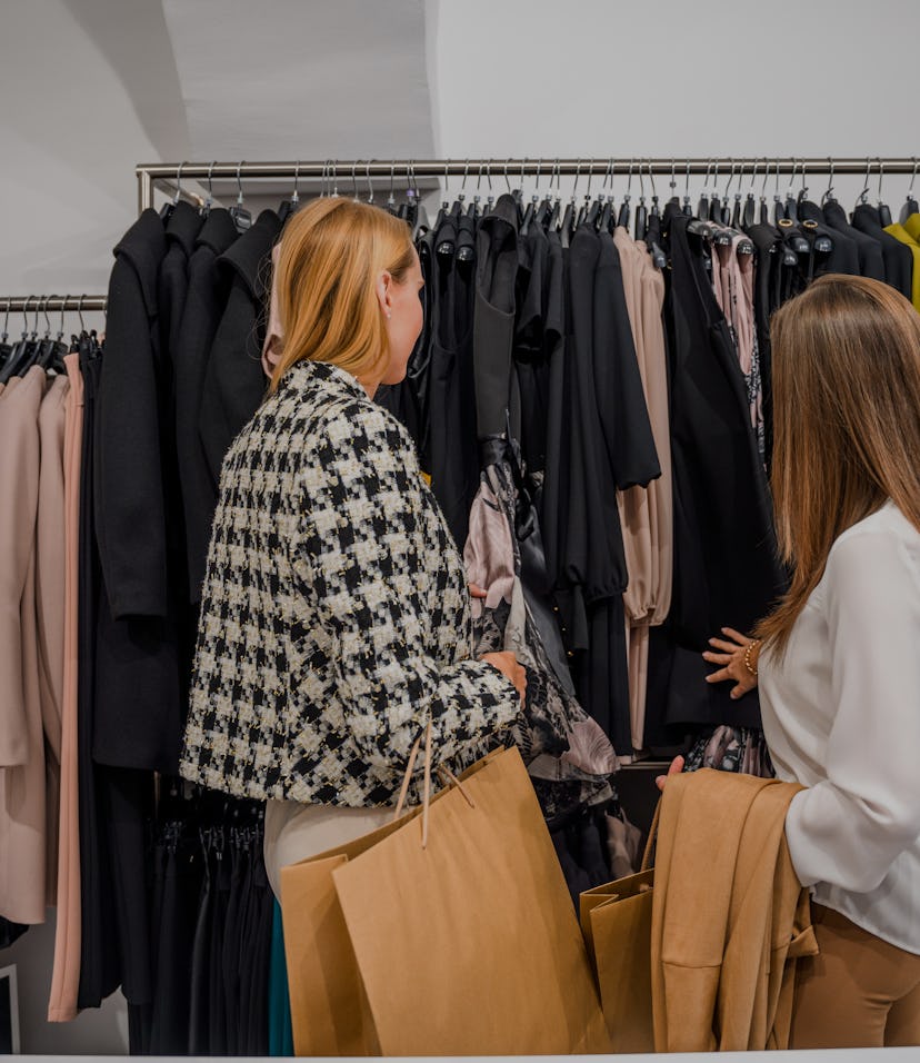 Two young female fashion buffs checking a clothing rack at a trendy fashion shop. 3/4 length image, ...