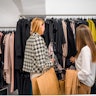 Two young female fashion buffs checking a clothing rack at a trendy fashion shop. 3/4 length image, ...
