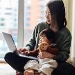 A mom looking at her computer with her baby on her lap. A new survey found that the averrage America...